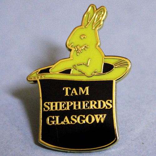 Black and yellow enamel shop logo (rabbit in a top hat) pin badge with raised gold lettering reads 'tam shepherds glasgow'. 21mm width by 30mm height